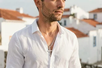 Homme portant une croix en argent sur chaîne longue avec chemise en lin blanc, décor côtier portugais